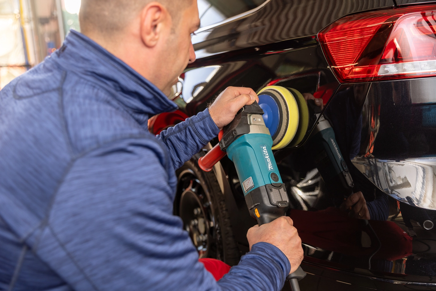 BlitzSauber das Reinigungszentrum Rellingen UG - Fahrzeugpflege - Mann poliert mit einem Makita-Akkuschrauber die Rückseite eines schwarzen Autos